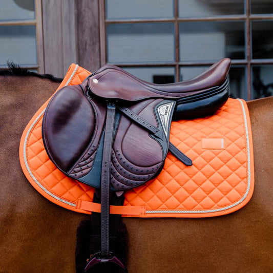 orange saddle pad on a bay horse in a stable yard