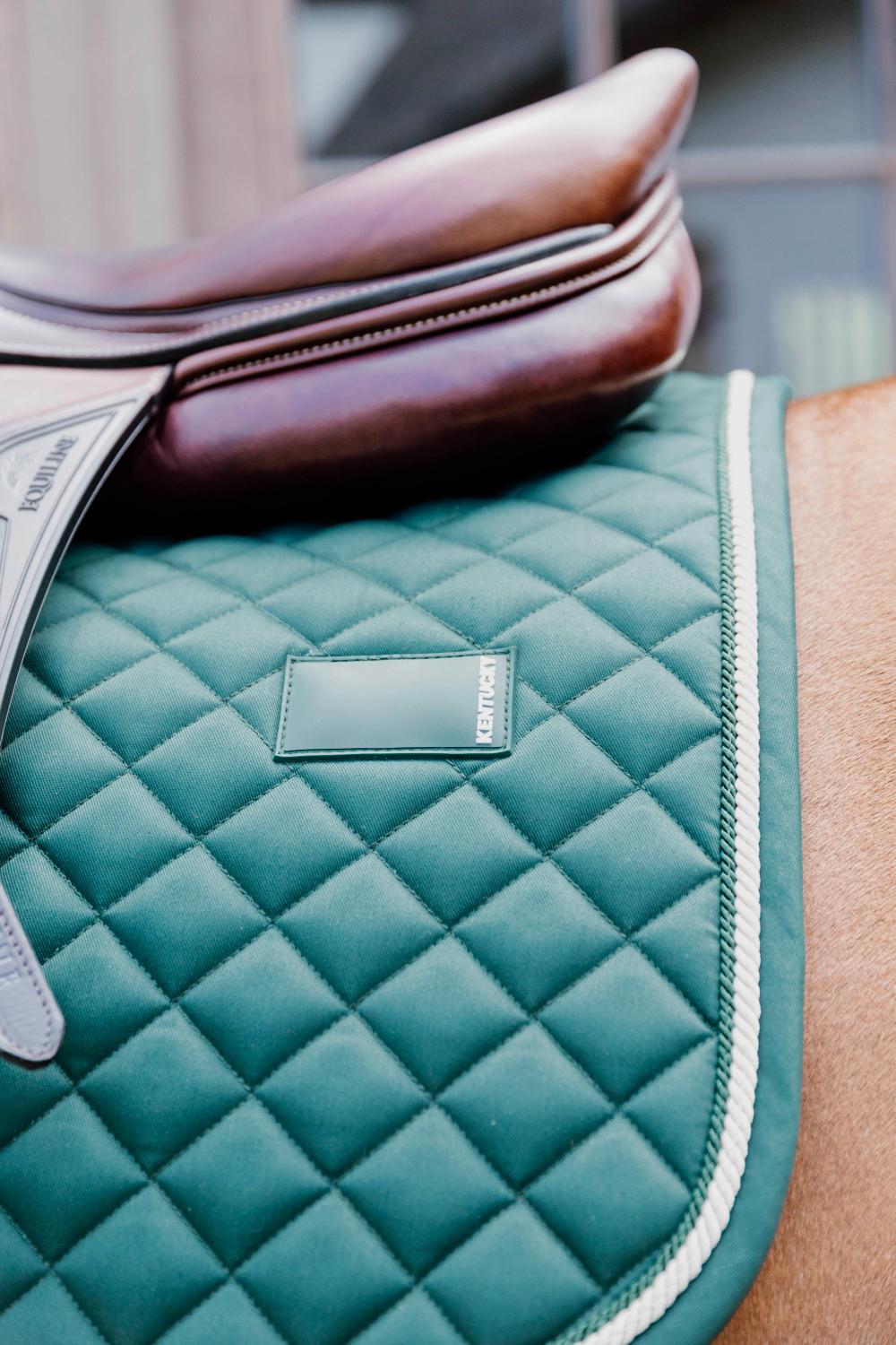 Teal quilted saddle pad with a brand label on a horse saddle