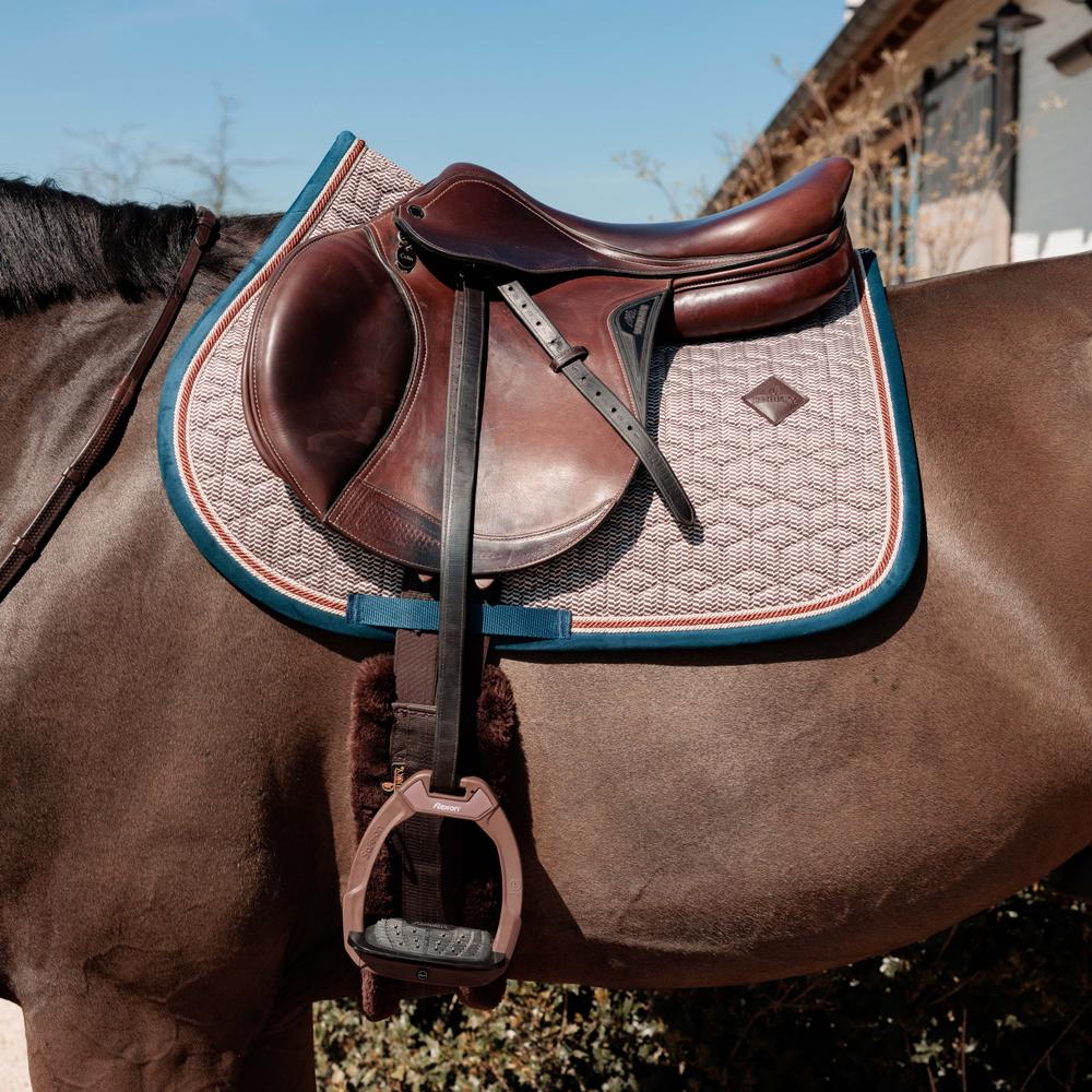 Brown horse with a leather saddle and blue girth strap on a clear day.