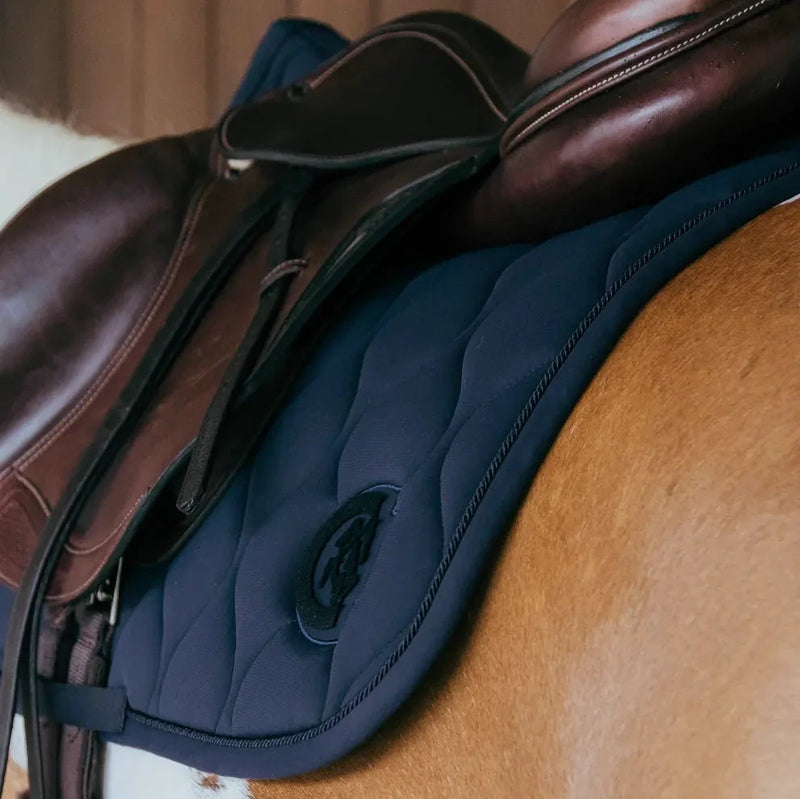 Close-up of a brown leather saddle with a blue saddle pad on a wooden surface.