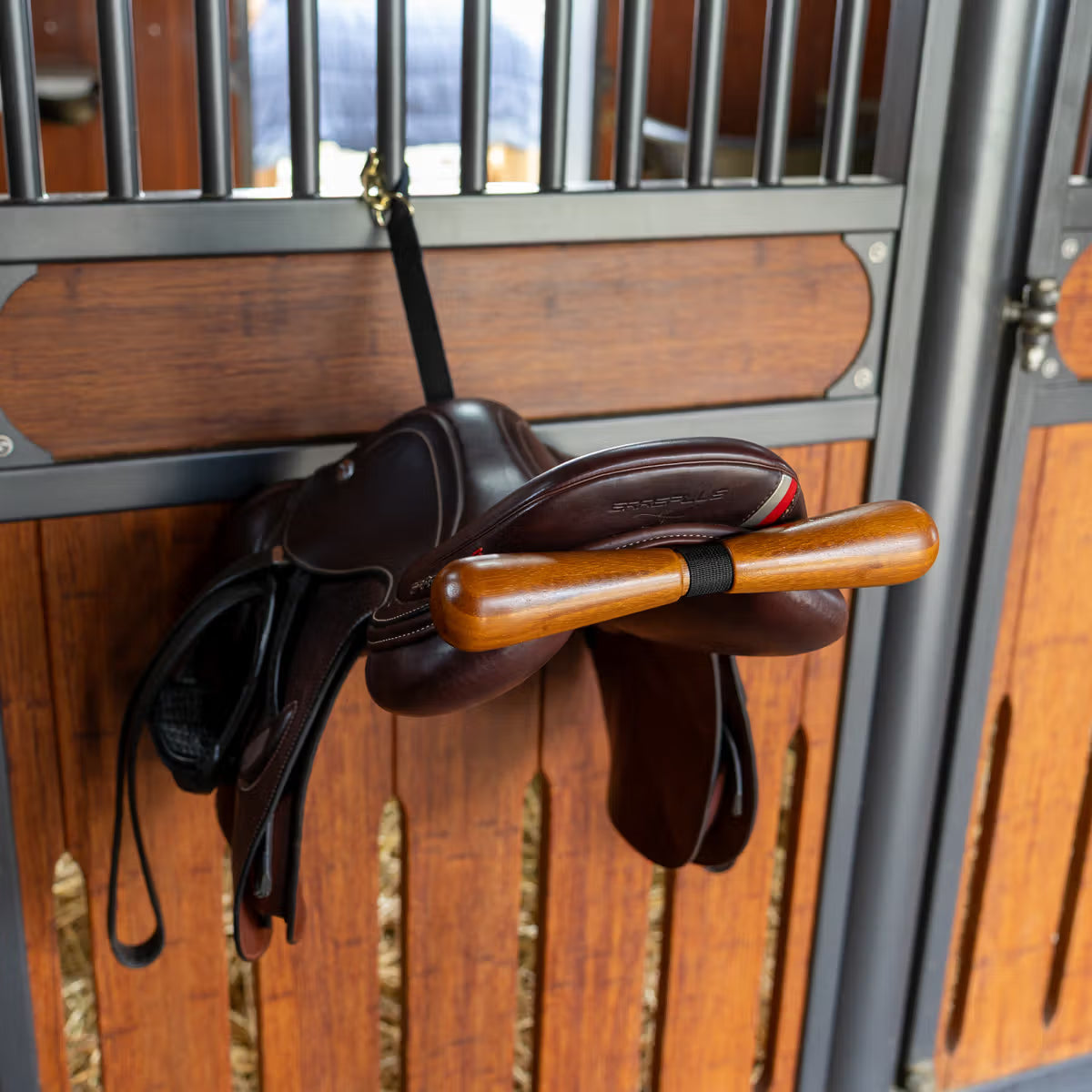 Brown leather saddle with wooden girth on a wooden stable door.