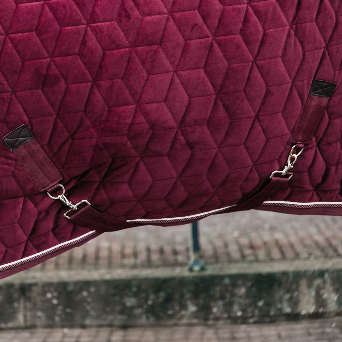 Close-up of a quilted purple saddle pad with straps on a blurred background