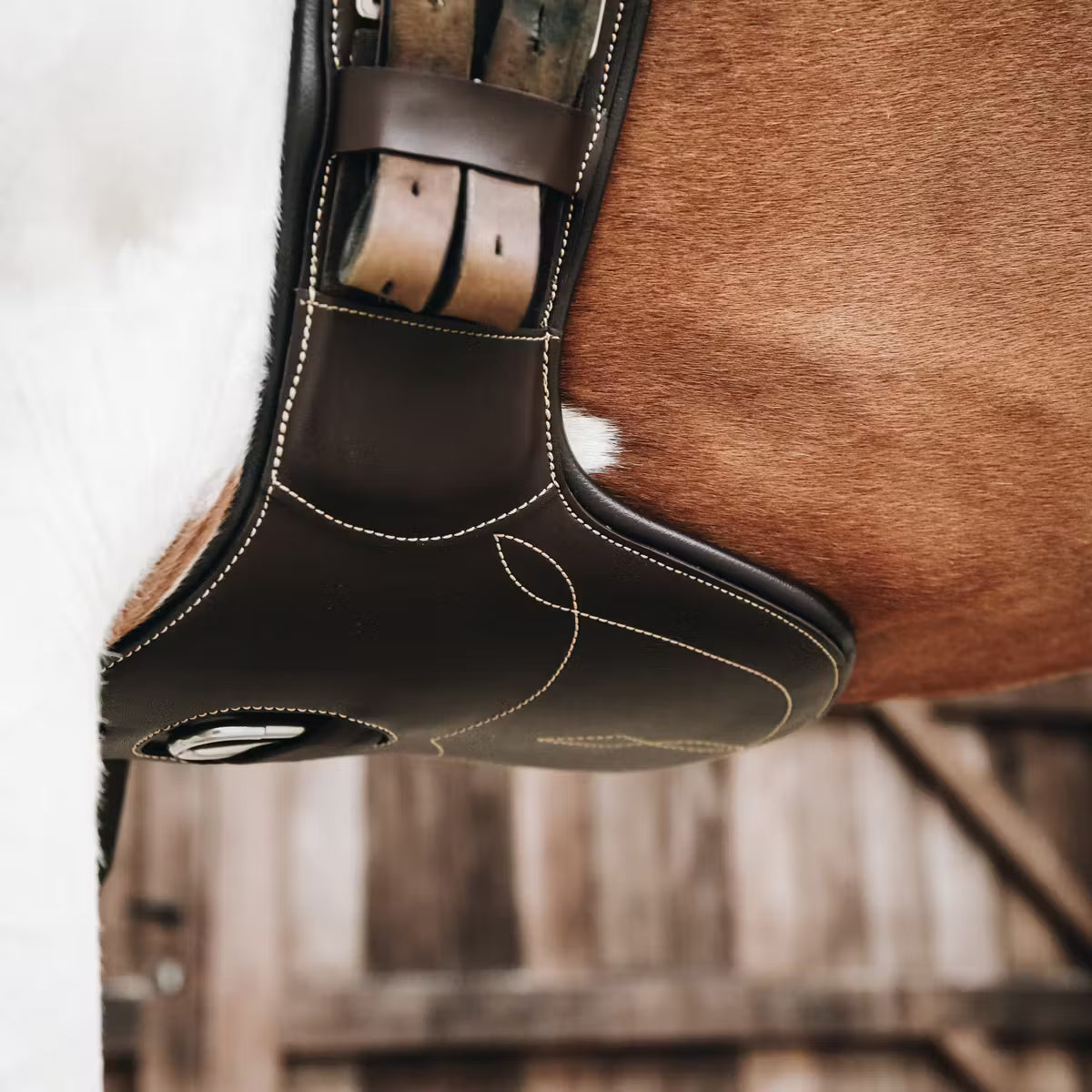 Close-up of a horse saddle pad on a horse, with a blurred wooden stable background.