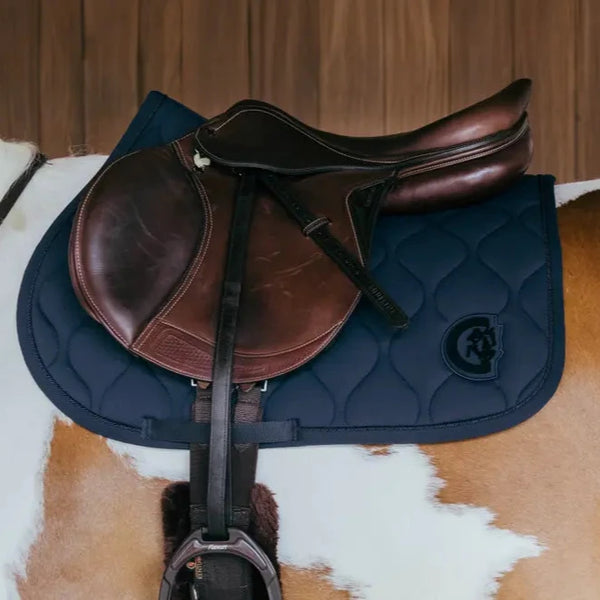 Brown leather saddle on a blue quilted saddle pad on a horse.