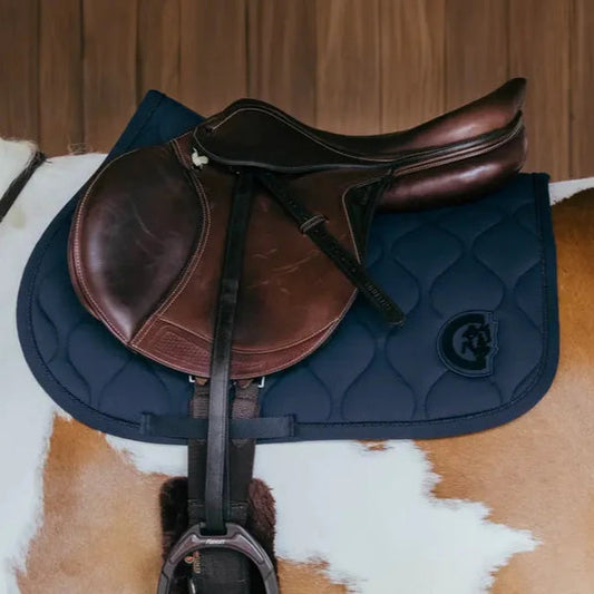 Brown leather saddle on a blue quilted saddle pad on a horse.