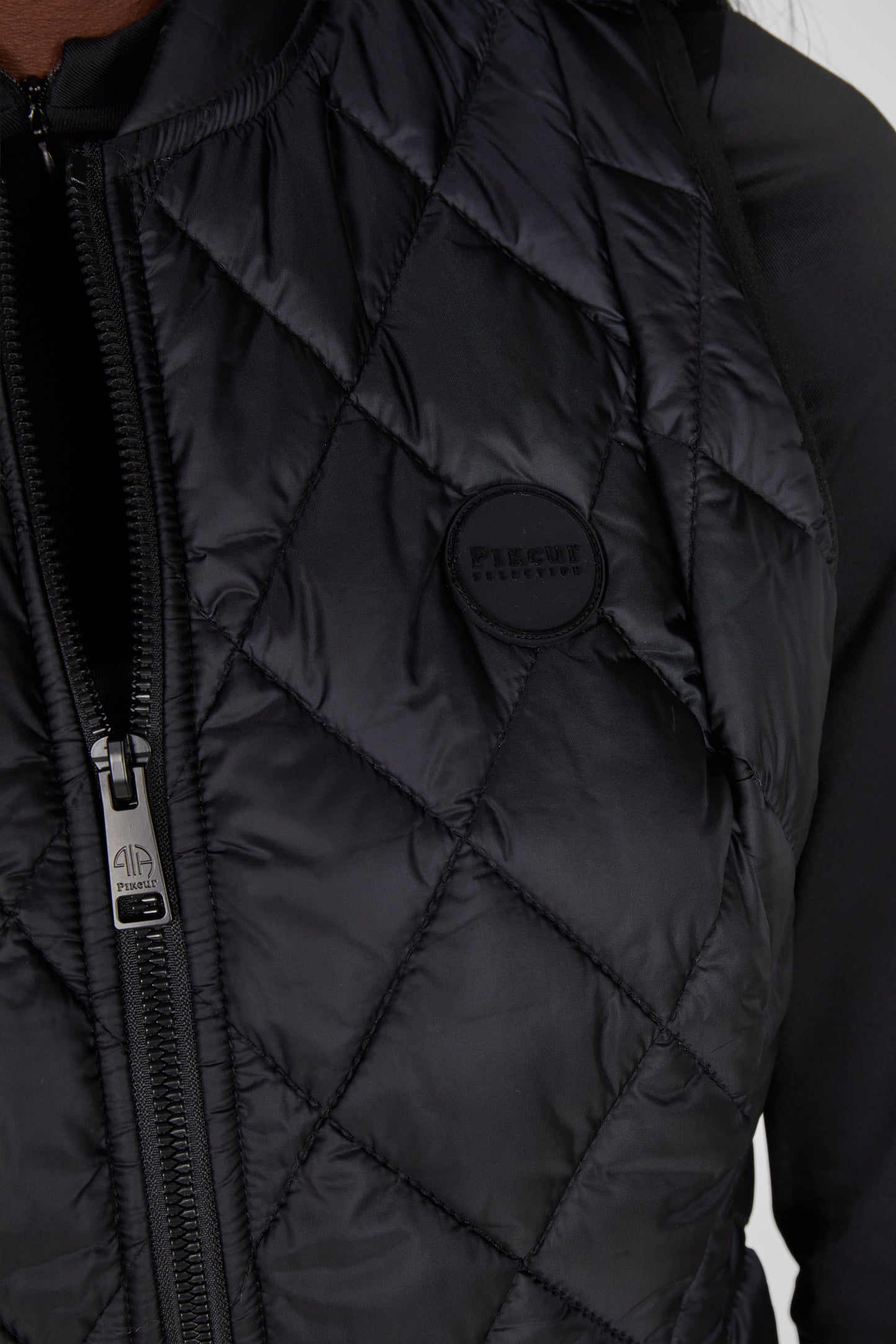 Close-up of a black quilted jacket with a brand logo on a neutral background