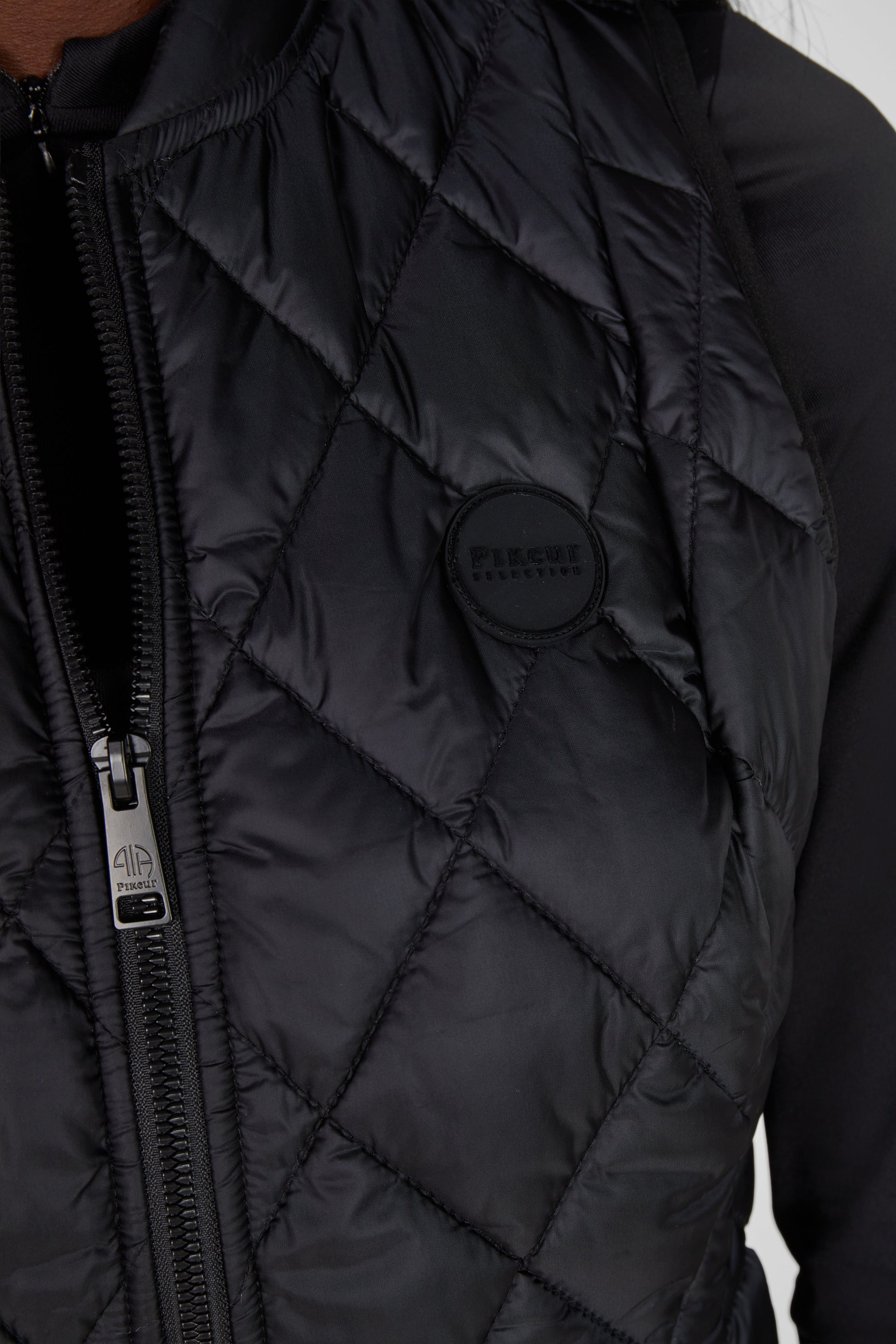 Close-up of a black quilted jacket with a brand logo on a neutral background