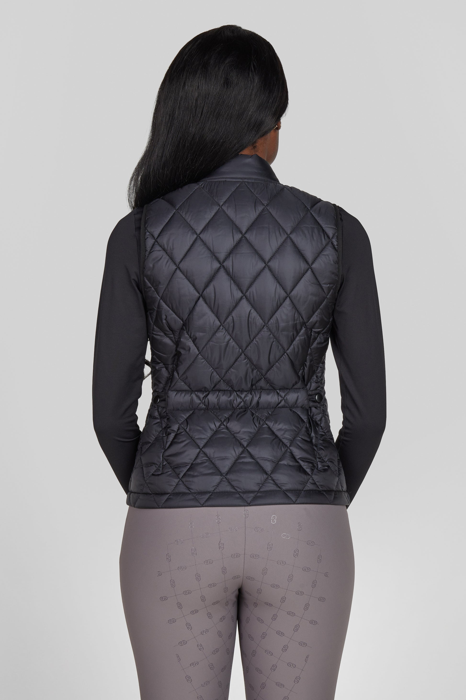 Person wearing a black quilted vest on a gray background