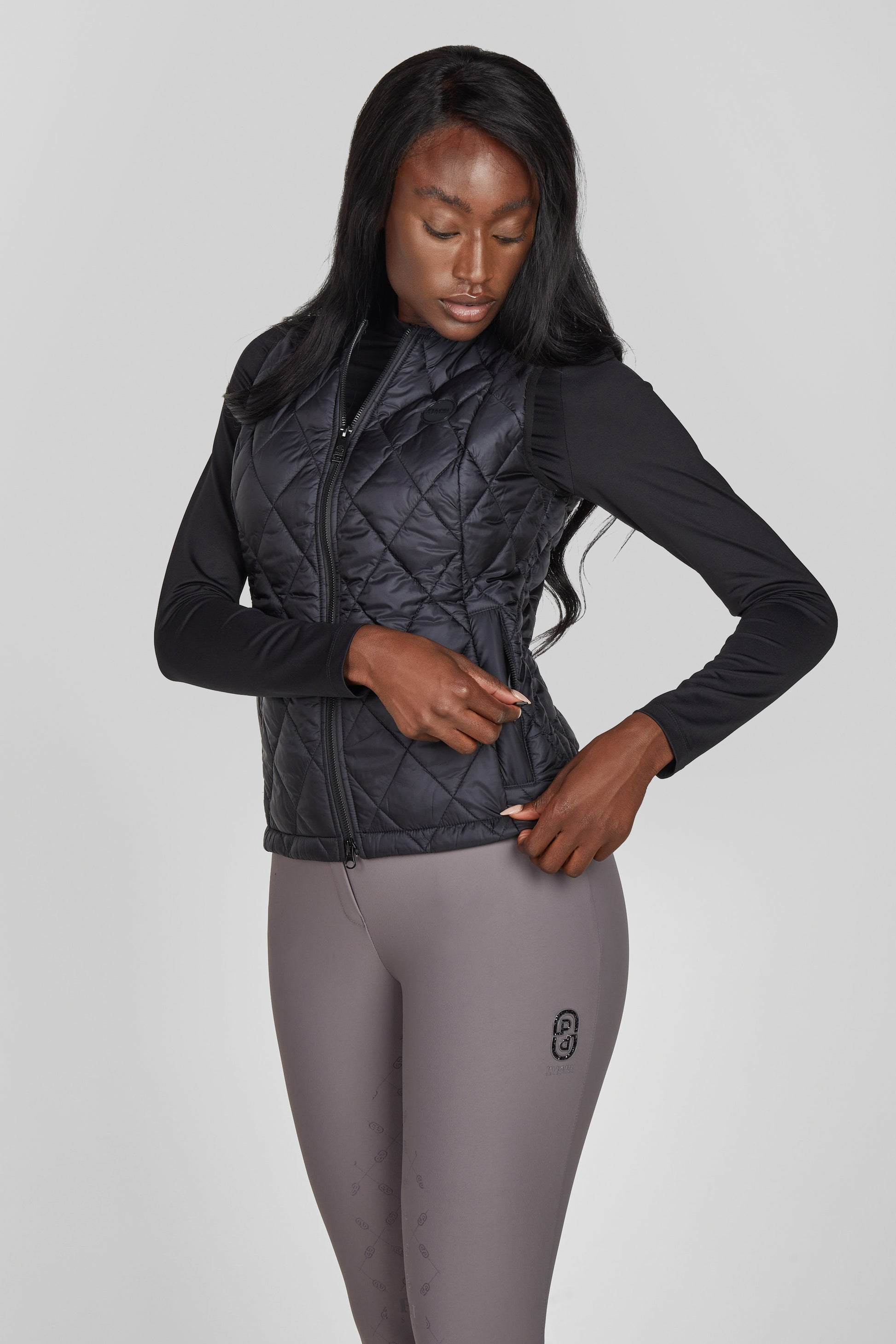 Woman wearing a black quilted vest and gray leggings on a light gray background