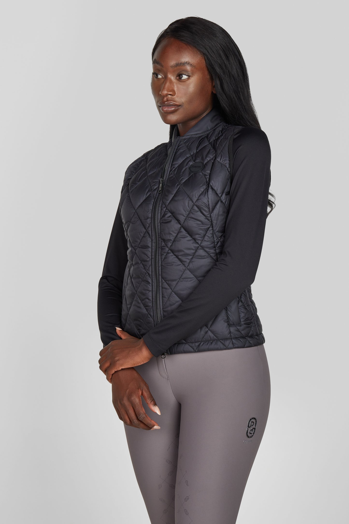 Woman wearing a black quilted jacket and gray leggings on a light gray background
