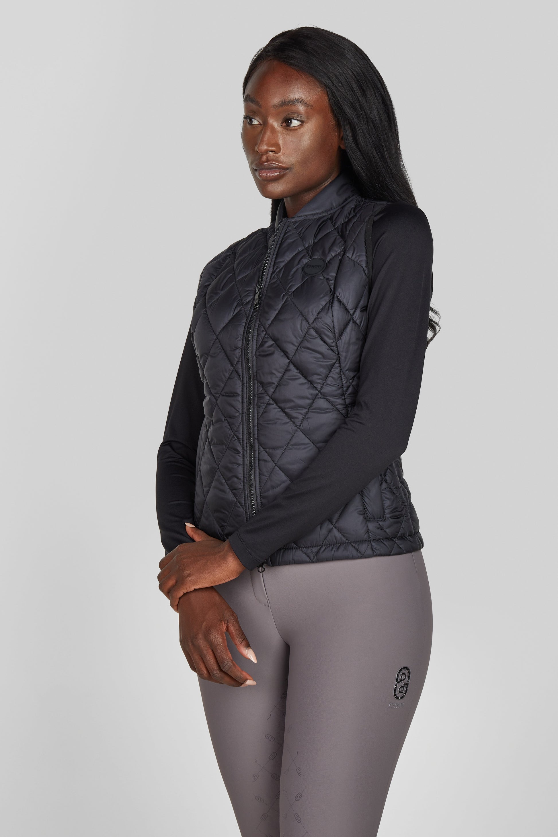 Woman wearing a black quilted jacket and gray leggings on a light gray background