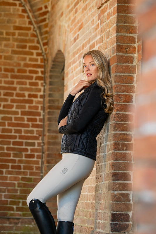 Woman in black jacket and gray leggings leaning against a brick wall.