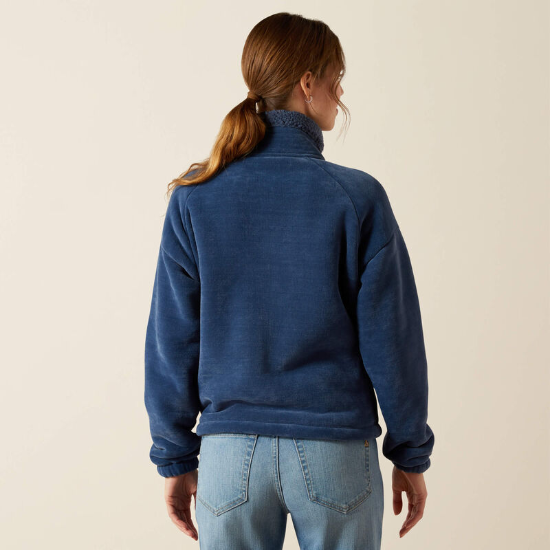 Person wearing a blue fleece jacket and jeans on a beige background