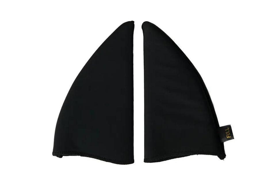 A pair of black neoprene shark fin wing covers, shown flat against a solid white background. A small black fabric tag with yellow text is attached to the lower right edge of the right fin.