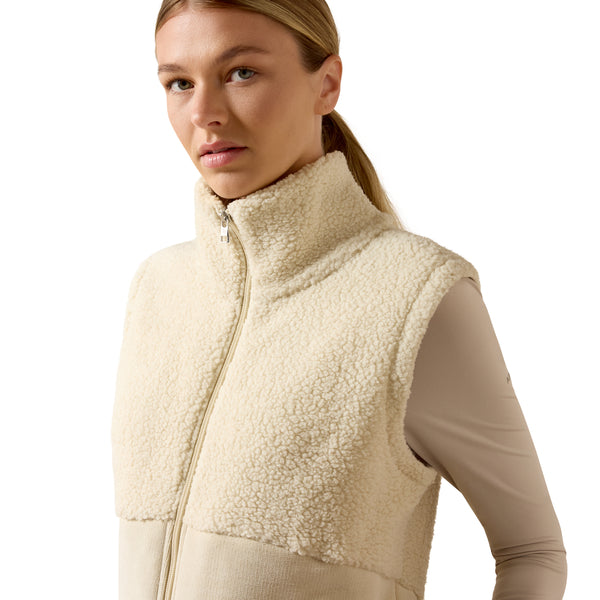 A woman wearing a cream sherpa fleece zip-up vest over a beige long-sleeve athletic top, photographed against a clean white studio background.