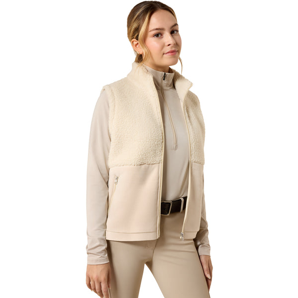 A woman modeling a beige fleece-lined zip-front vest over a matching beige long-sleeve top and beige pants, shown against a plain white studio background.