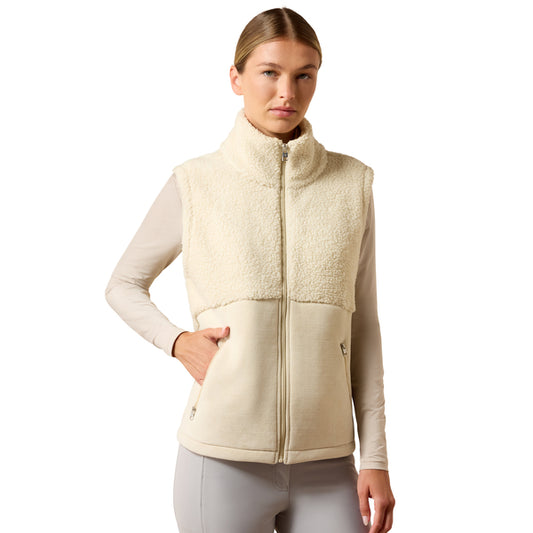 A woman modeling a cream sherpa fleece vest over a light beige long-sleeve top and gray leggings, photographed against a solid white background.