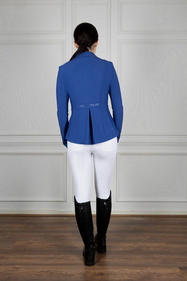 Person wearing a blue equestrian jacket, white pants, and black boots against a neutral background
