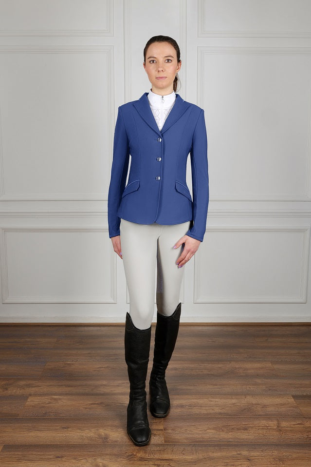 Person wearing a blue equestrian jacket, white shirt, beige pants, and black boots against a plain background.