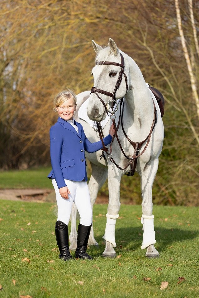 Young girl in equestrian attire standing next to a white horse on a grassy field.