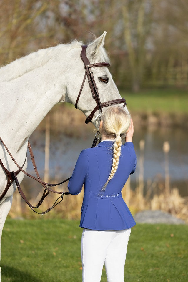 Young girl in equestrian attire standing next to a white horse on a grassy field.