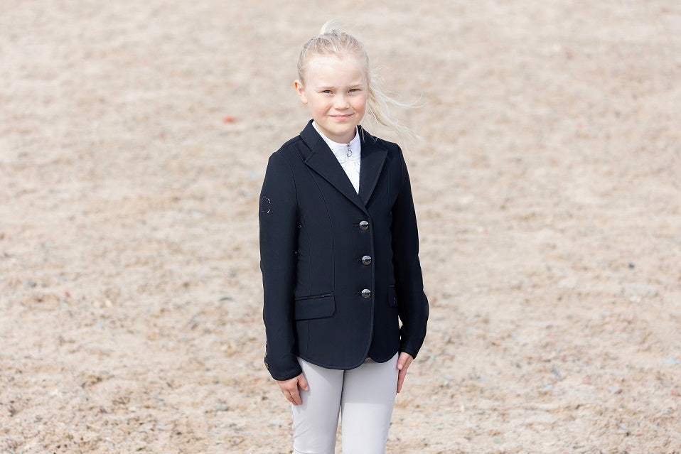 Young girl wearing a navy equestrian jacket on a beige background