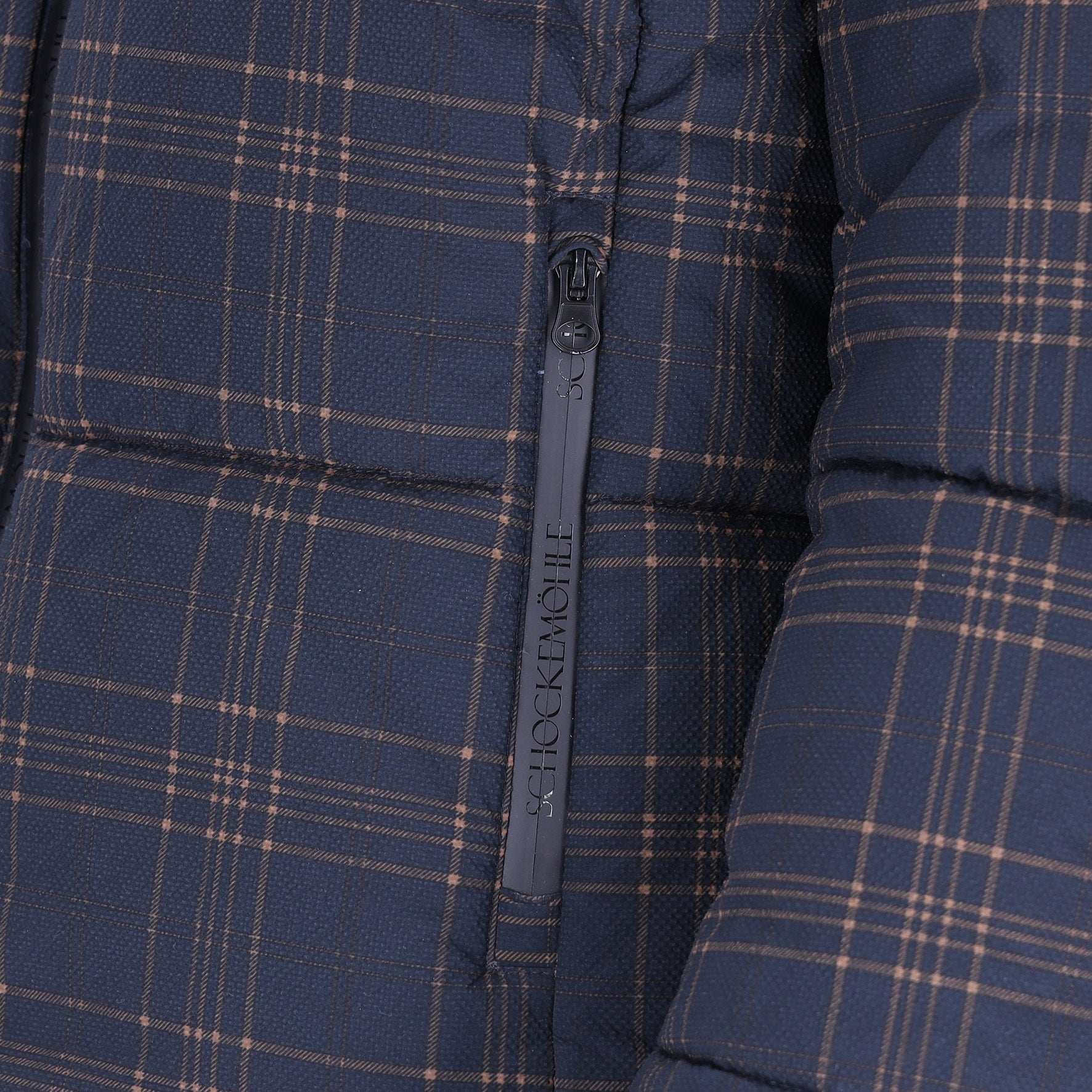 Close-up of a navy blue puffer jacket with a tan and brown plaid pattern, featuring a dark gray zipper with the brand name 'SCHOCKEMÖHLE' printed vertically.
