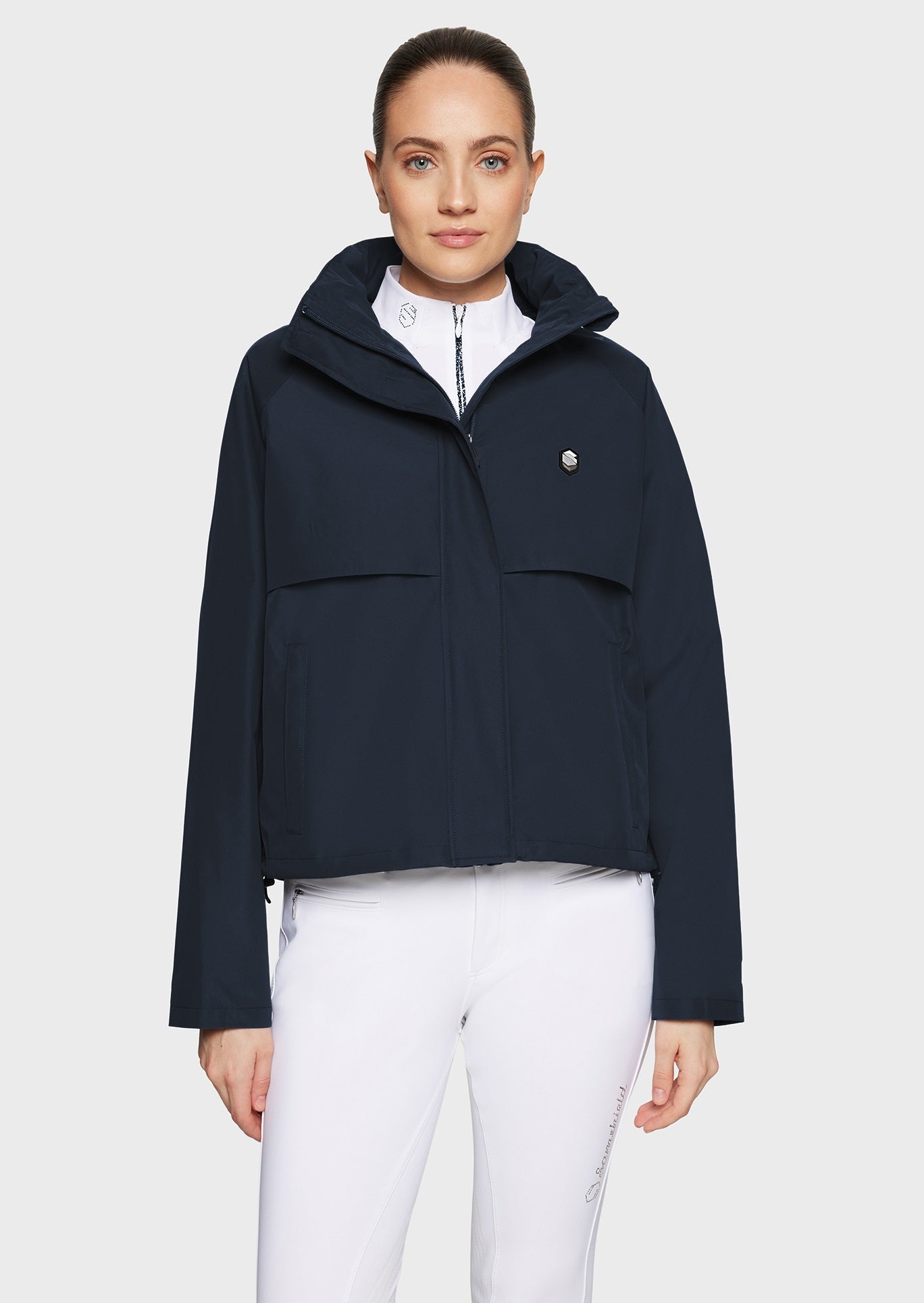 Woman wearing a navy jacket and white breeches on a beige background