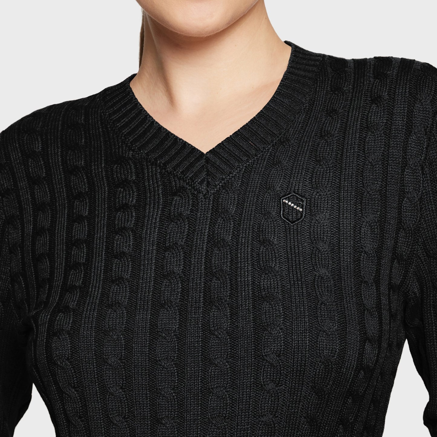 Black cable knit sweater with a brand logo on a light gray background