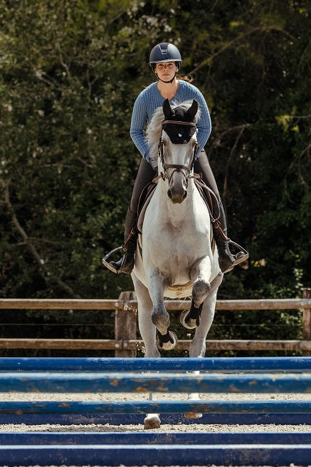 Person riding a white horse over an obstacle with a dark green background