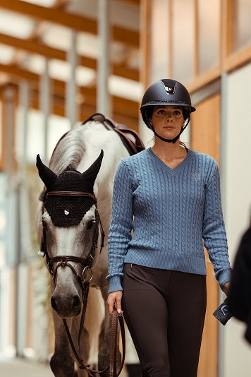 Woman in equestrian gear walking a horse in an indoor arena