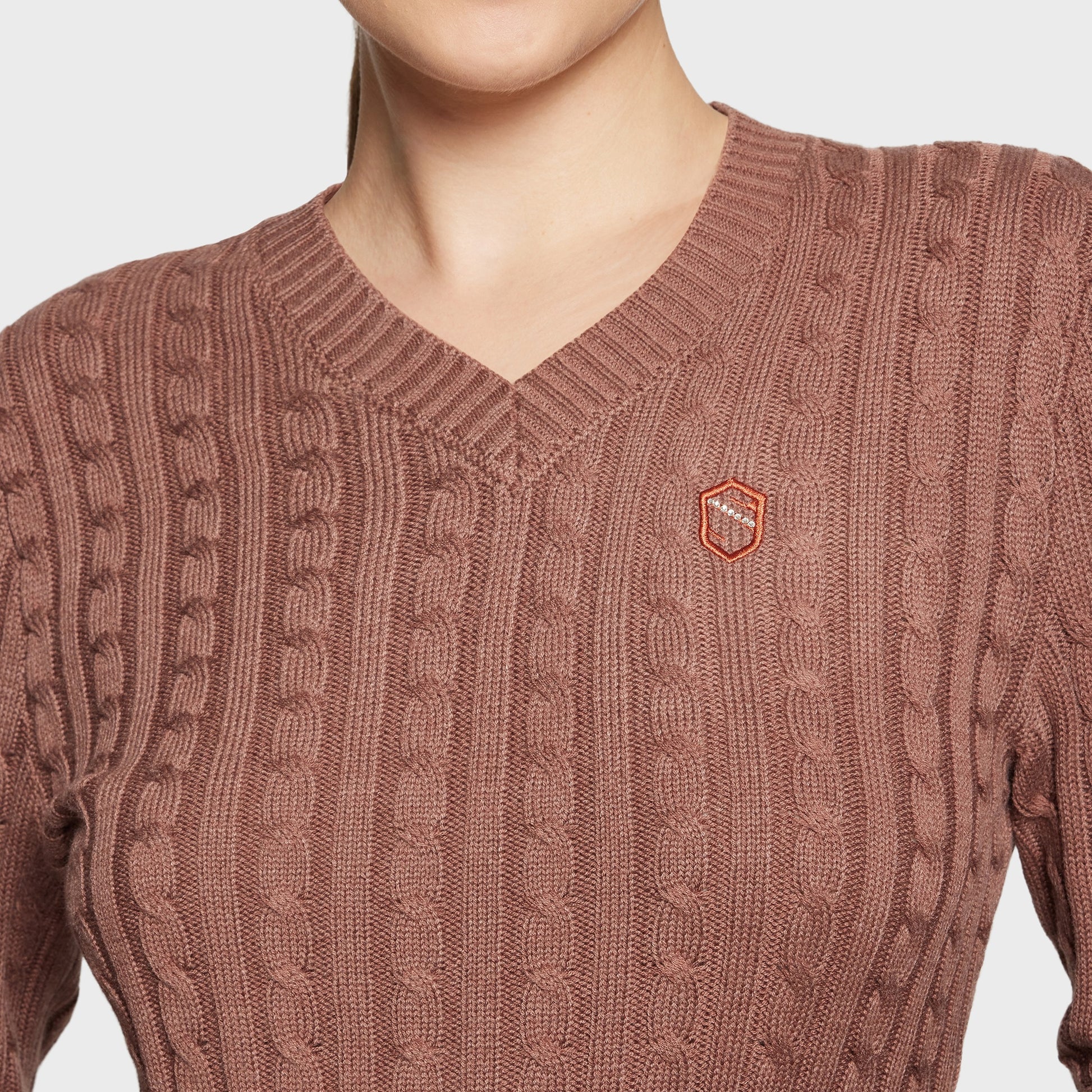 Brown cable knit sweater with a small logo on a light gray background