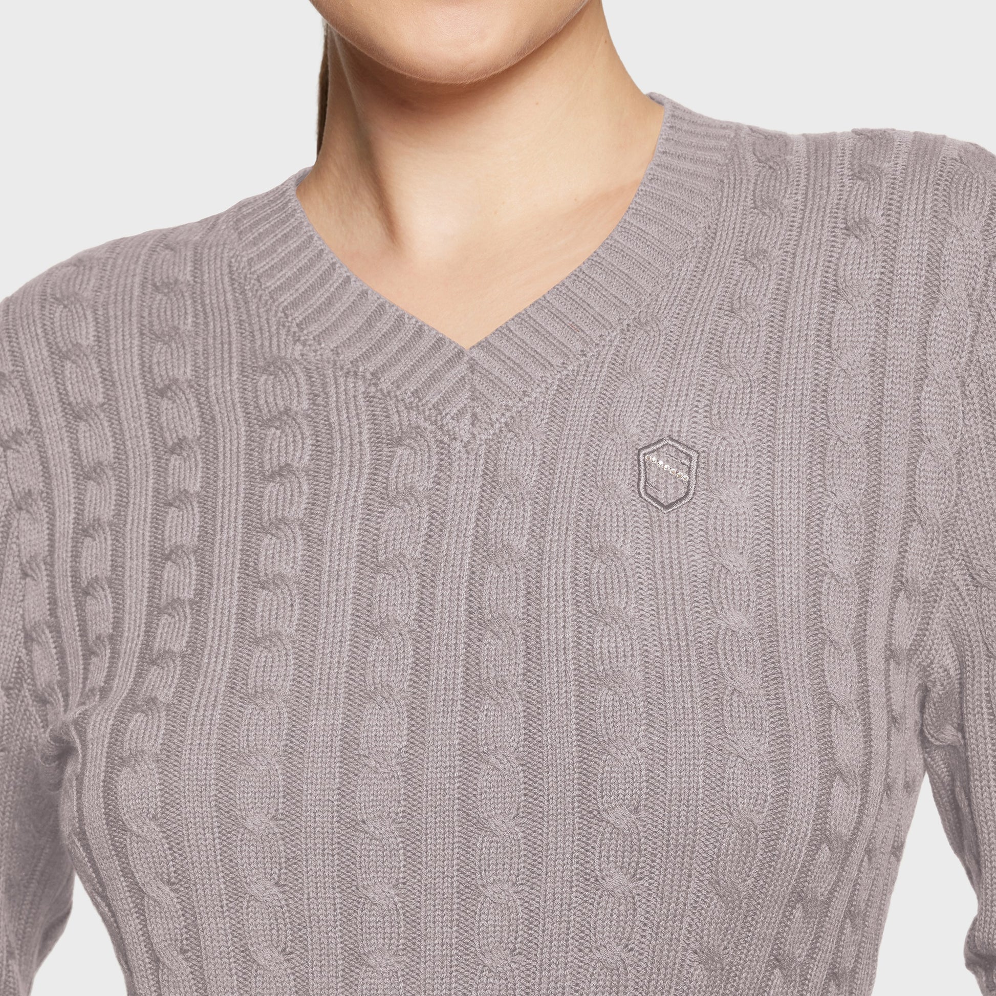 Close-up of a gray cable knit sweater with a brand logo on a light background