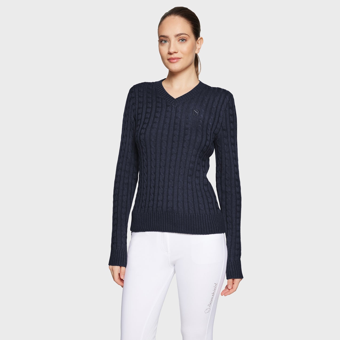 Woman wearing a navy blue cable knit sweater and white pants on a light gray background