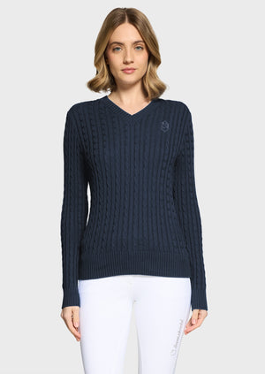 Woman wearing a navy jumper and white breeches on a beige background