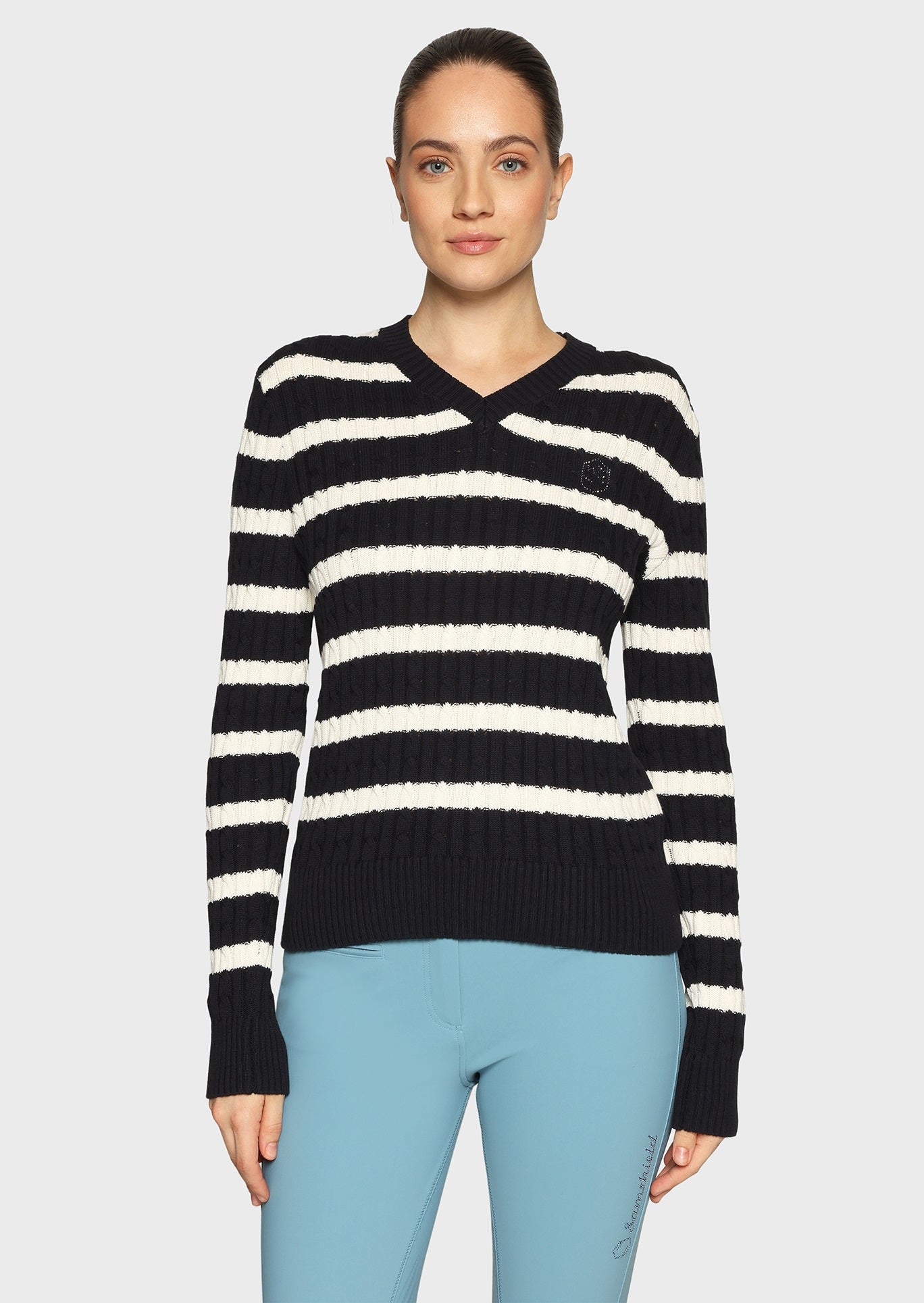 Woman wearing a white and navy striped jumper and blue breeches on a beige background