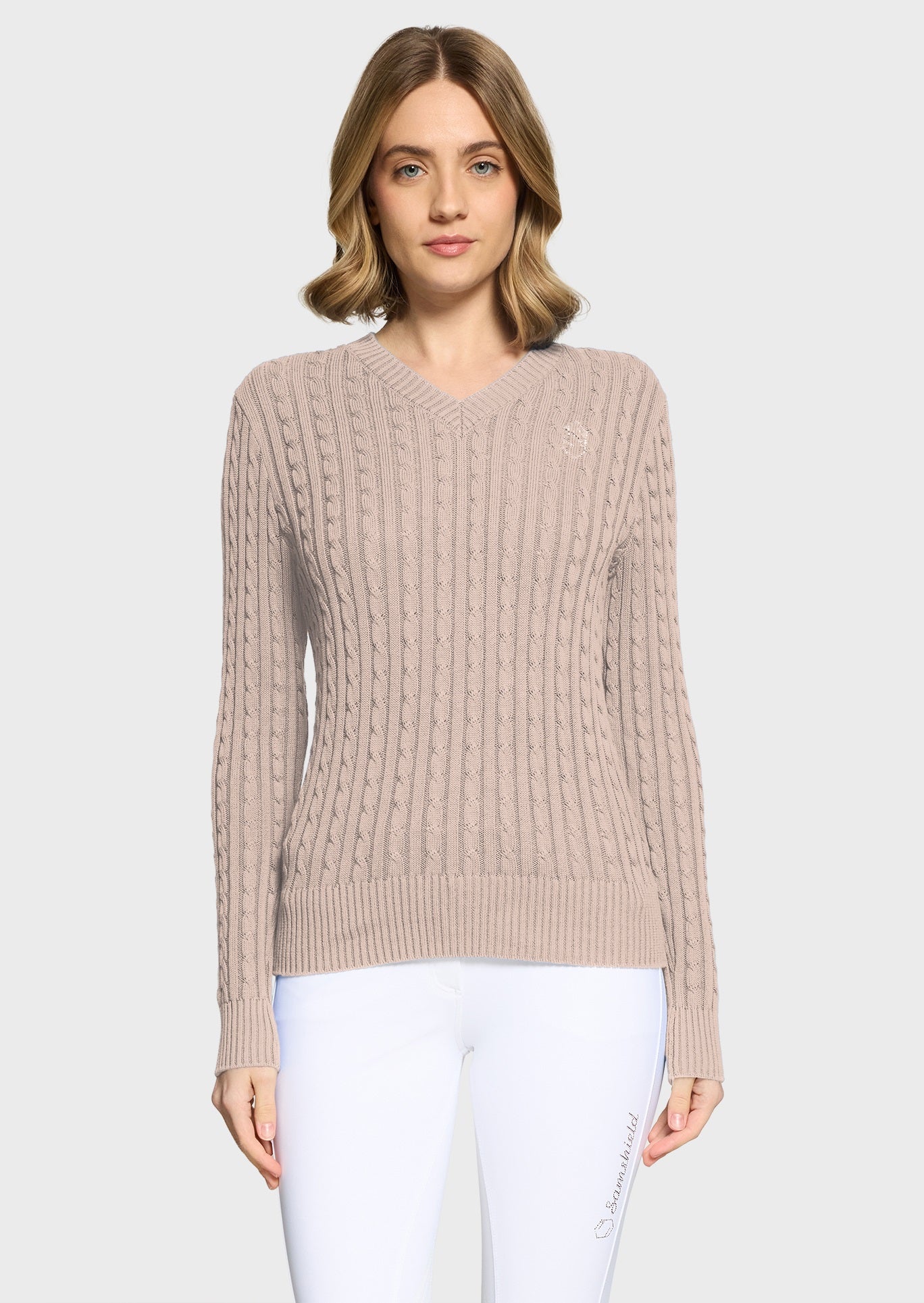 Woman wearing a pink jumper and white breeches on a beige background