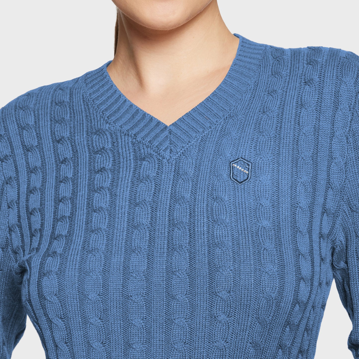 Blue cable knit sweater with a brand logo on a light gray background