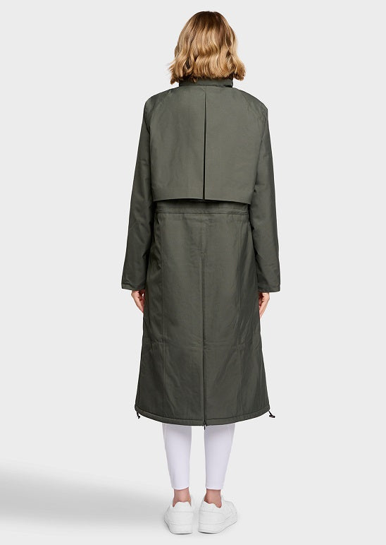 A model viewed from the back wearing a long olive green coat over white leggings and white sneakers, set against a plain light gray studio background.