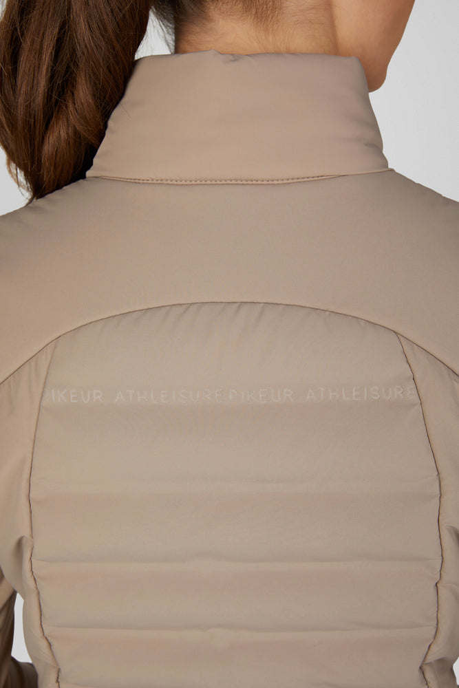 Close-up back view of a person wearing a beige puffer gilet with horizontal quilting and subtle tonal branding across the upper back.