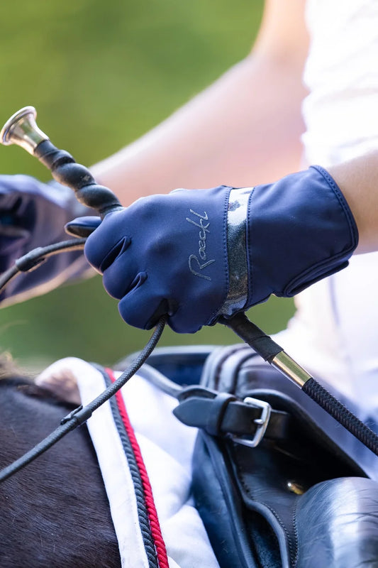 Person wearing a blue equestrian glove holding reins with a blurred background