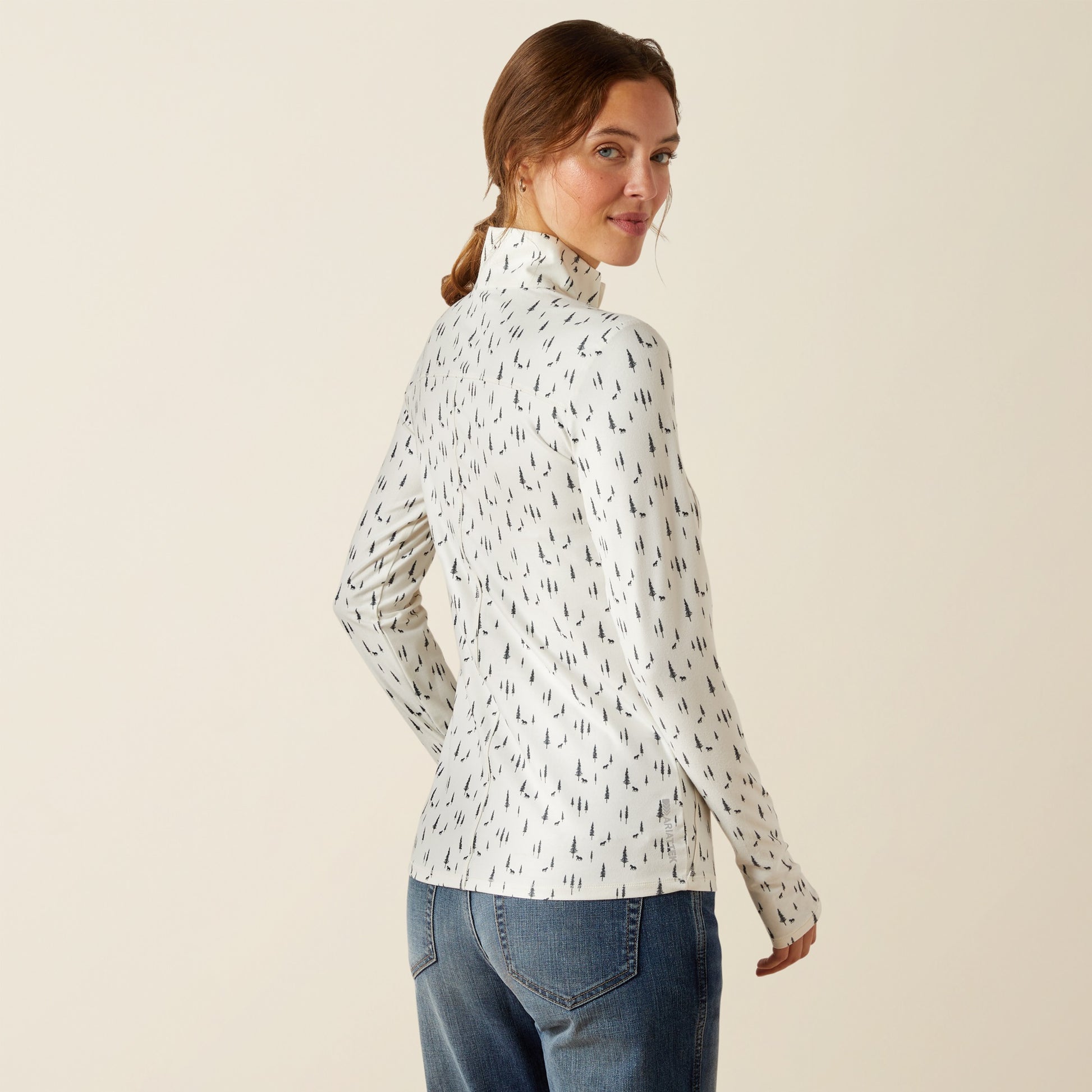 Woman wearing a white patterned long-sleeve shirt and blue jeans on a beige background