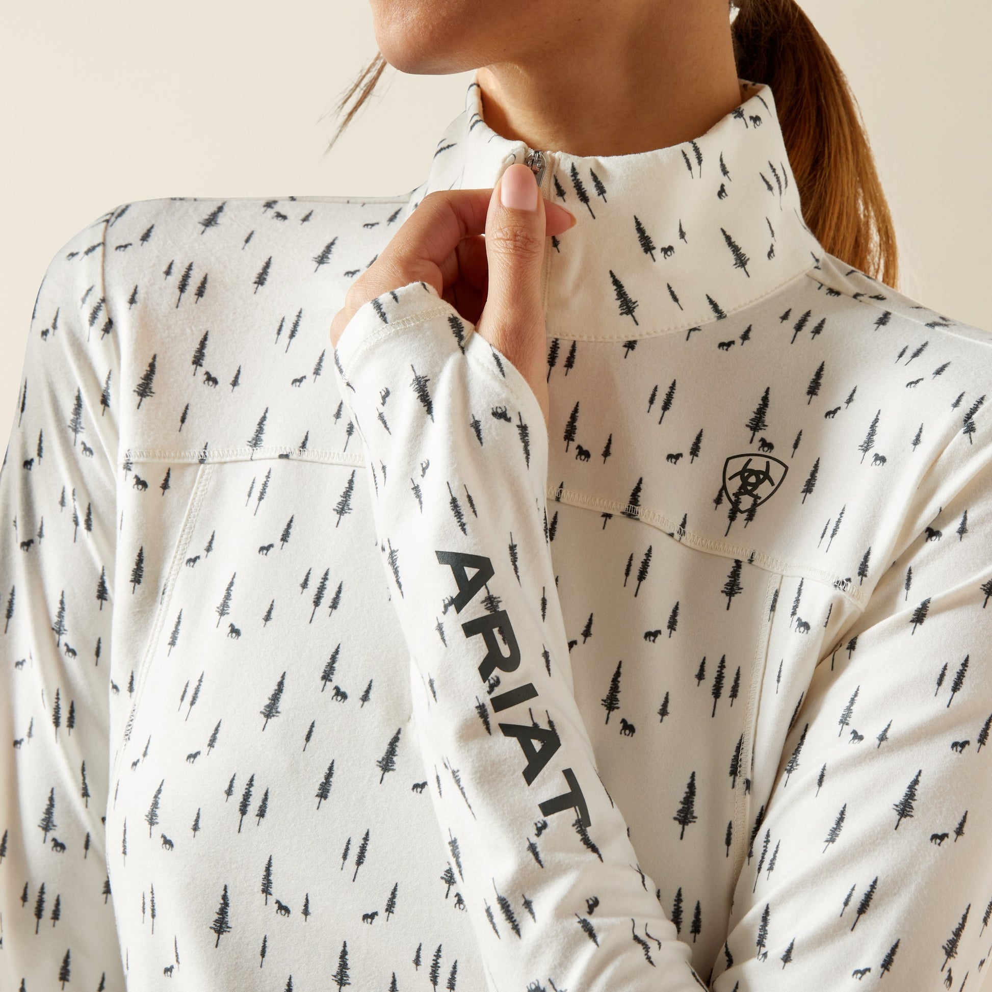 Person wearing a white long-sleeve shirt with black tree pattern and Ariat logo.