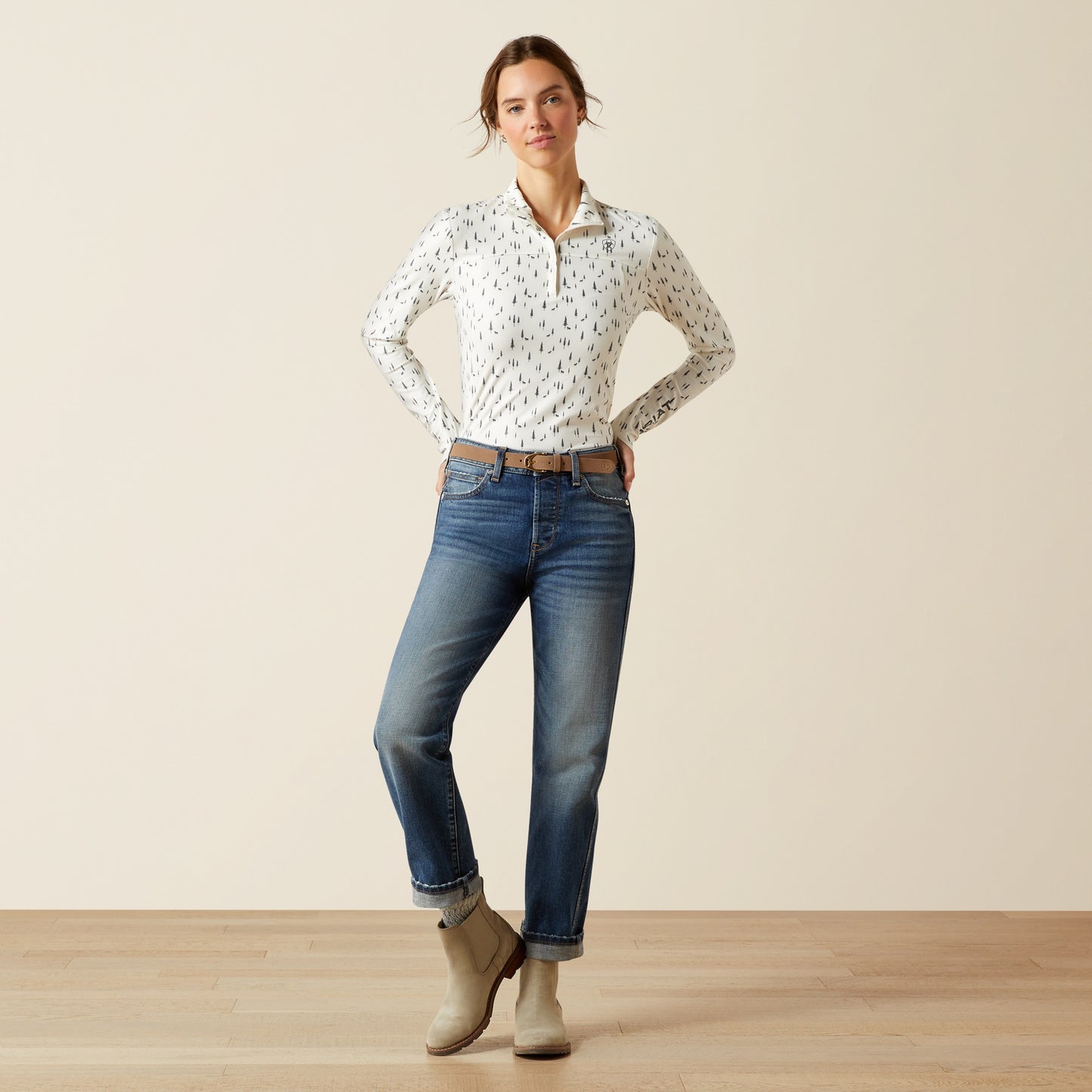 Woman wearing a patterned shirt, jeans, and boots on a plain background