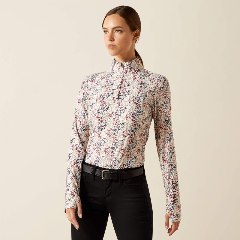 Woman wearing a patterned long-sleeve top and black pants on a beige background