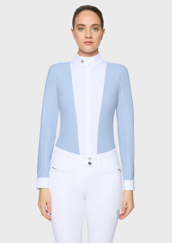 A woman shown from the back wearing a light blue long-sleeve equestrian-style top with a white collar and white fitted pants against a light gray studio background.