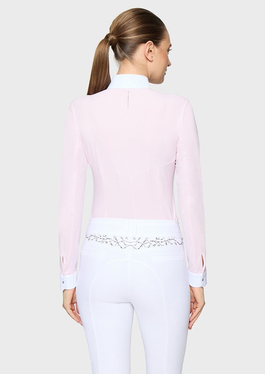 A woman shown from the back wearing a light pink long-sleeve equestrian-style top with a high mock neck and white fitted pants against a light gray studio background.