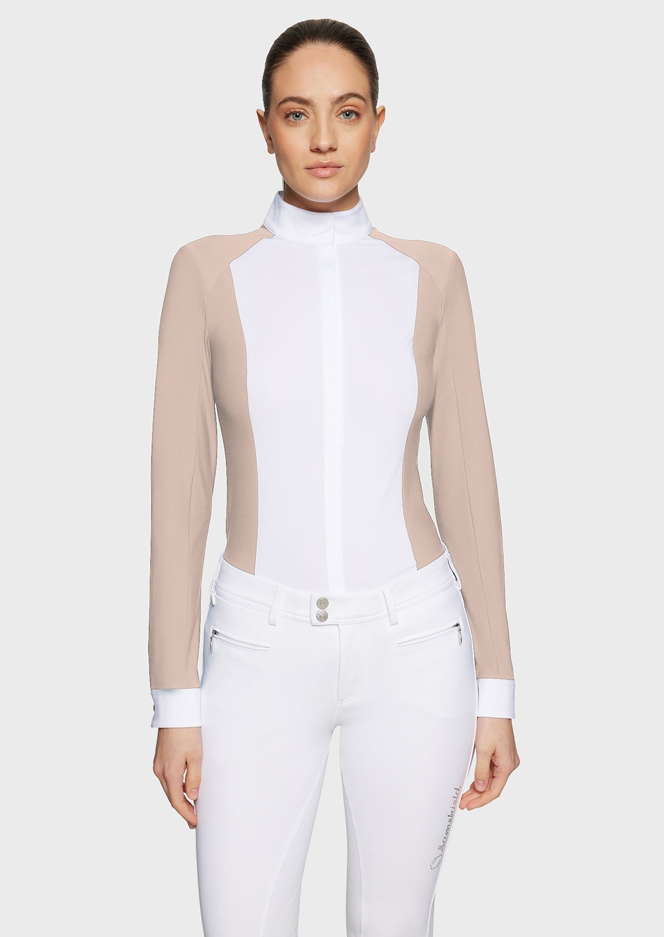 Woman wearing a pink competition shirt with a white bib and white breeches on a beige background