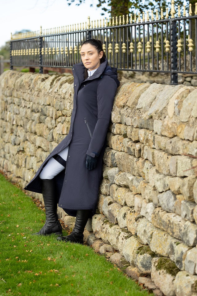 Woman in a dark coat leaning against a brick wall.