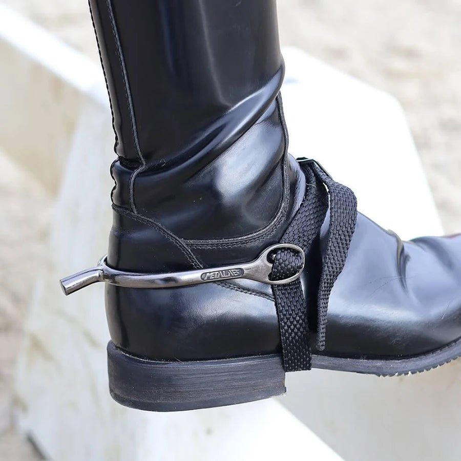 Close-up of a black equestrian boot with a metal spur and strap on a blurred background